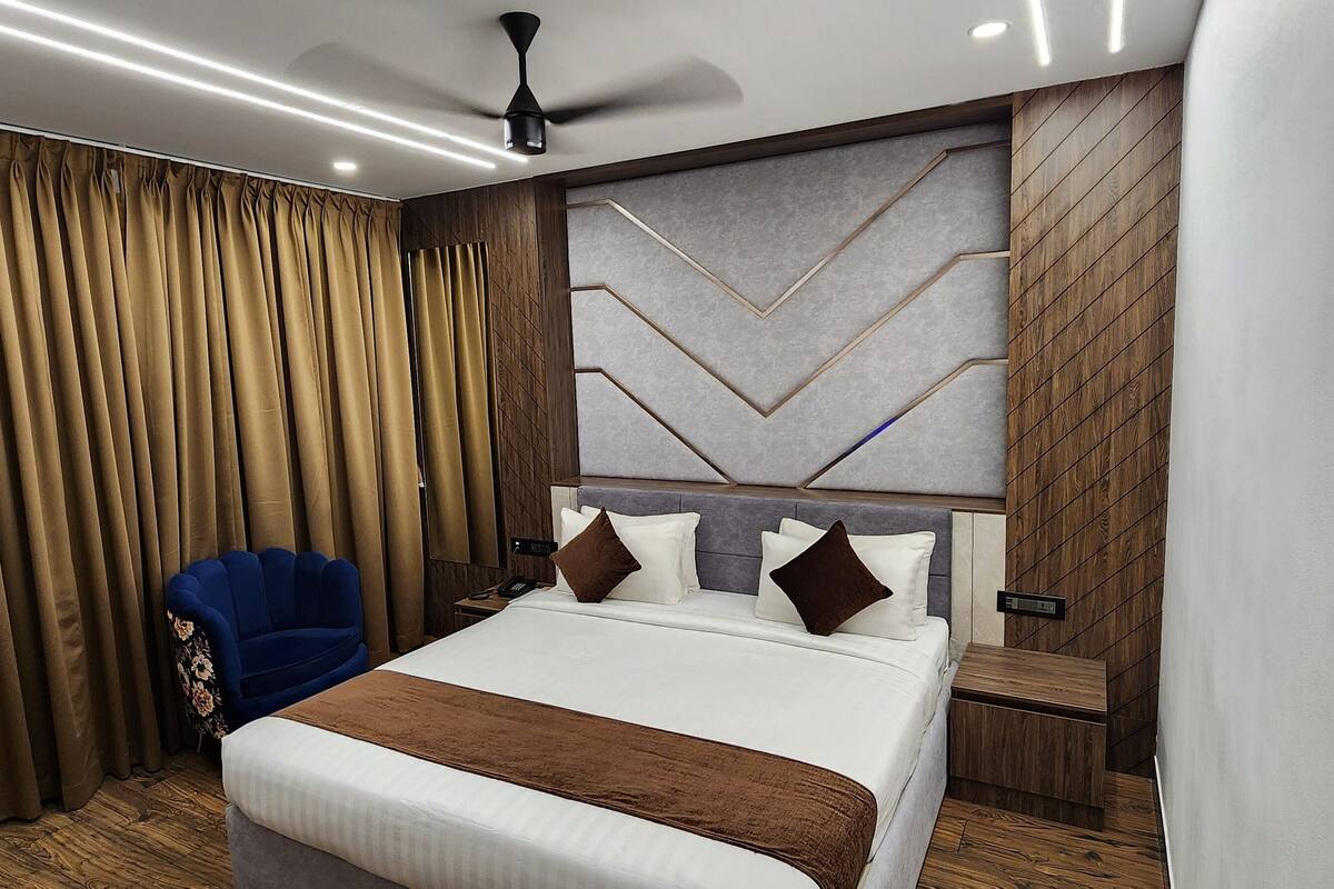 A modern hotel room with a large bed, a blue armchair, and a decorative wall panel.
