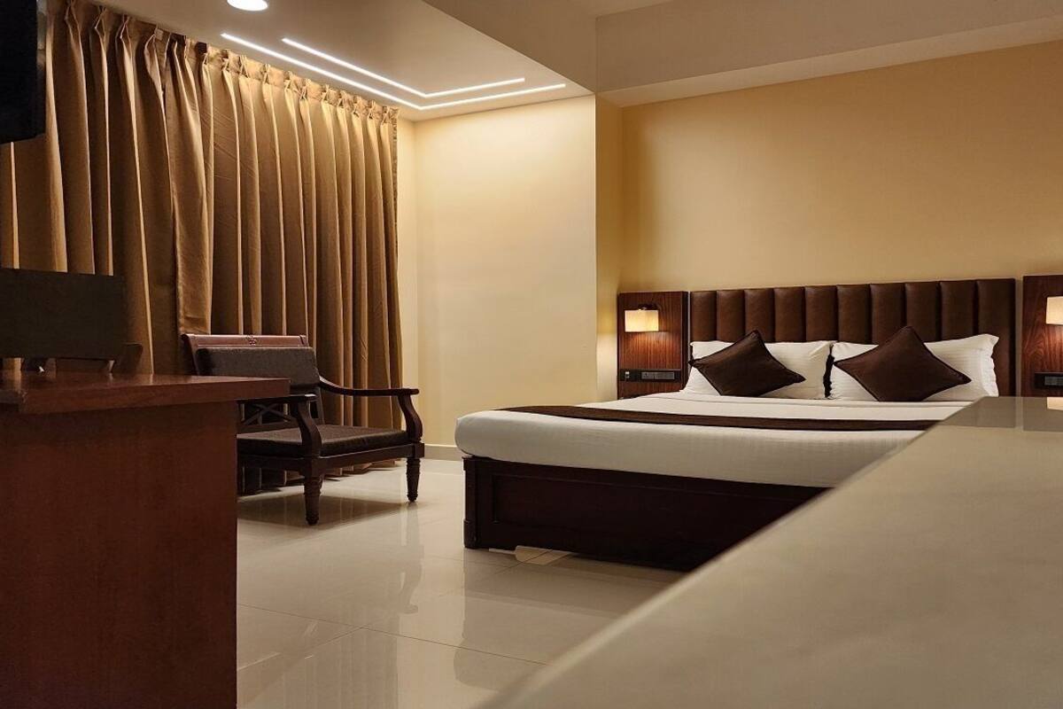 A hotel room with a large bed, two bedside tables with lamps, a desk with a chair, and a curtain.