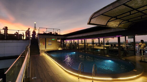 A pool area with a glass enclosure, a pool, and a view of the sunset.