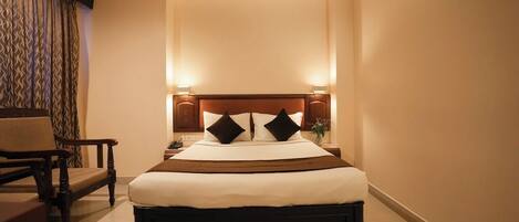 Een verzorgde hotelkamer met een groot bed, nachtlampjes, een stoel en een klein tafeltje.