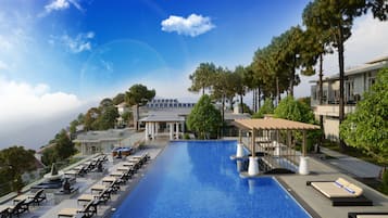 Relax by the rectangular pool surrounded by lush greenery and lounge areas with sunbeds and umbrellas.