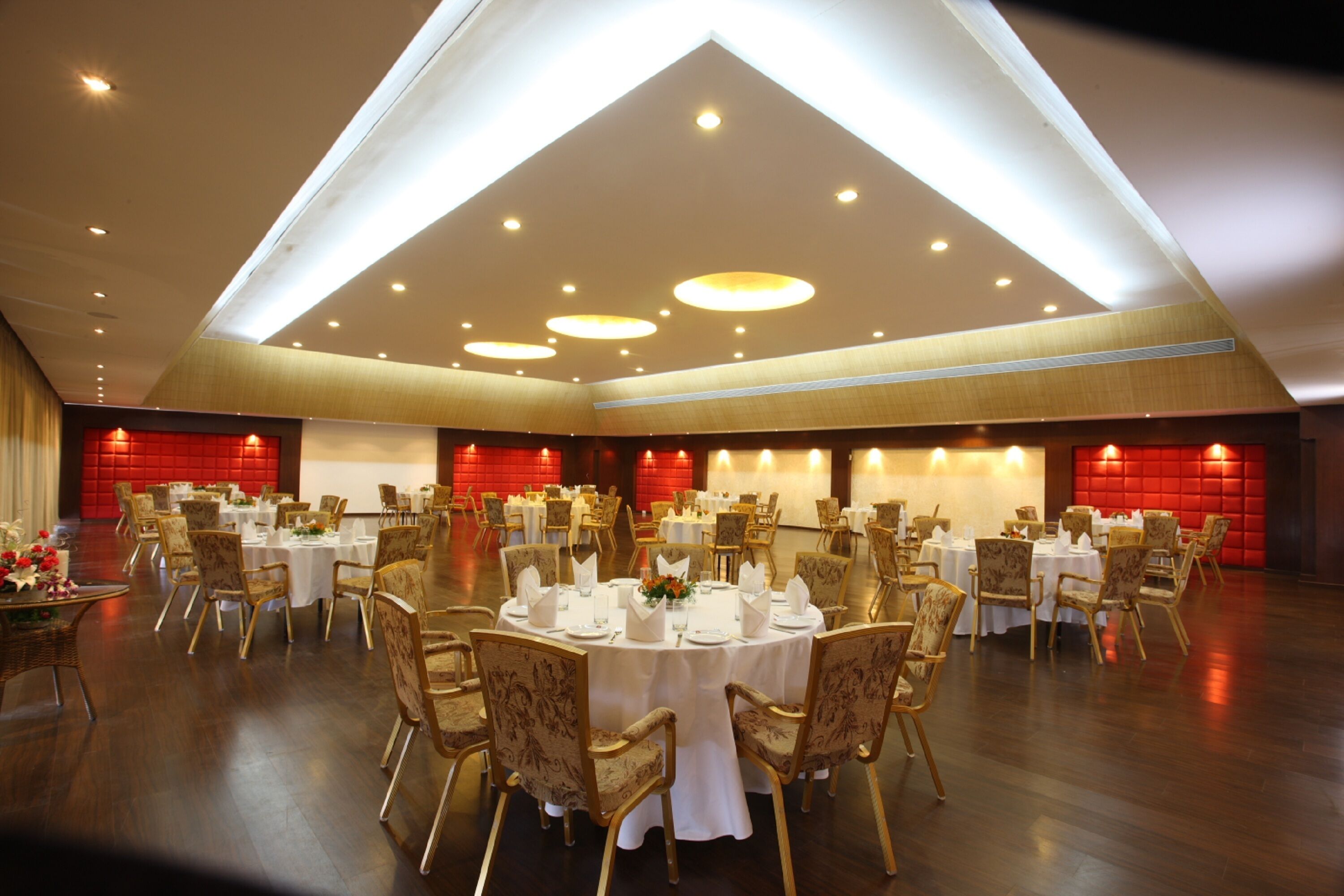 A banquet hall with round tables, chairs, and a red accent wall.