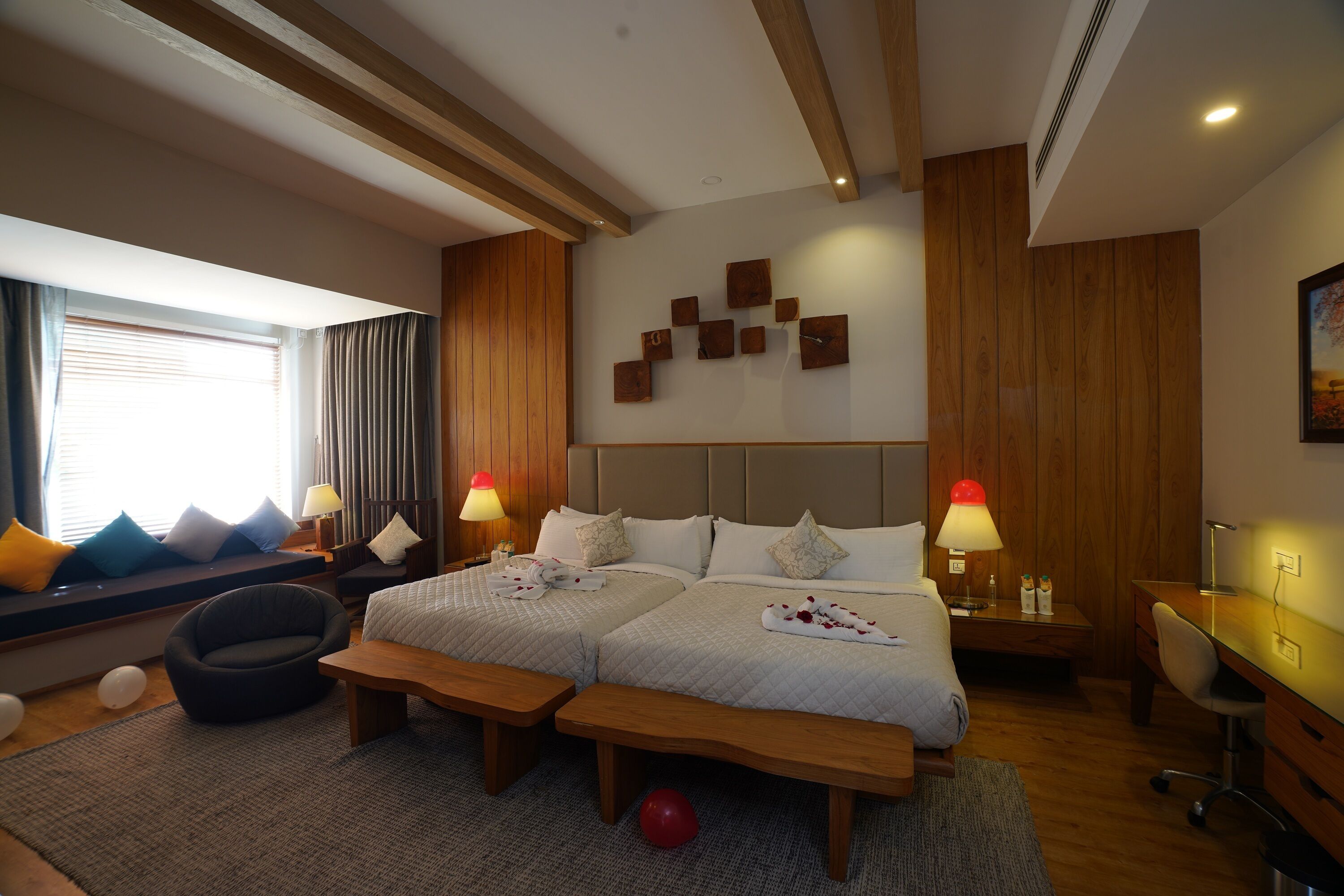 A hotel room with two beds, a desk, a chair, a sofa, and a window with curtains.
