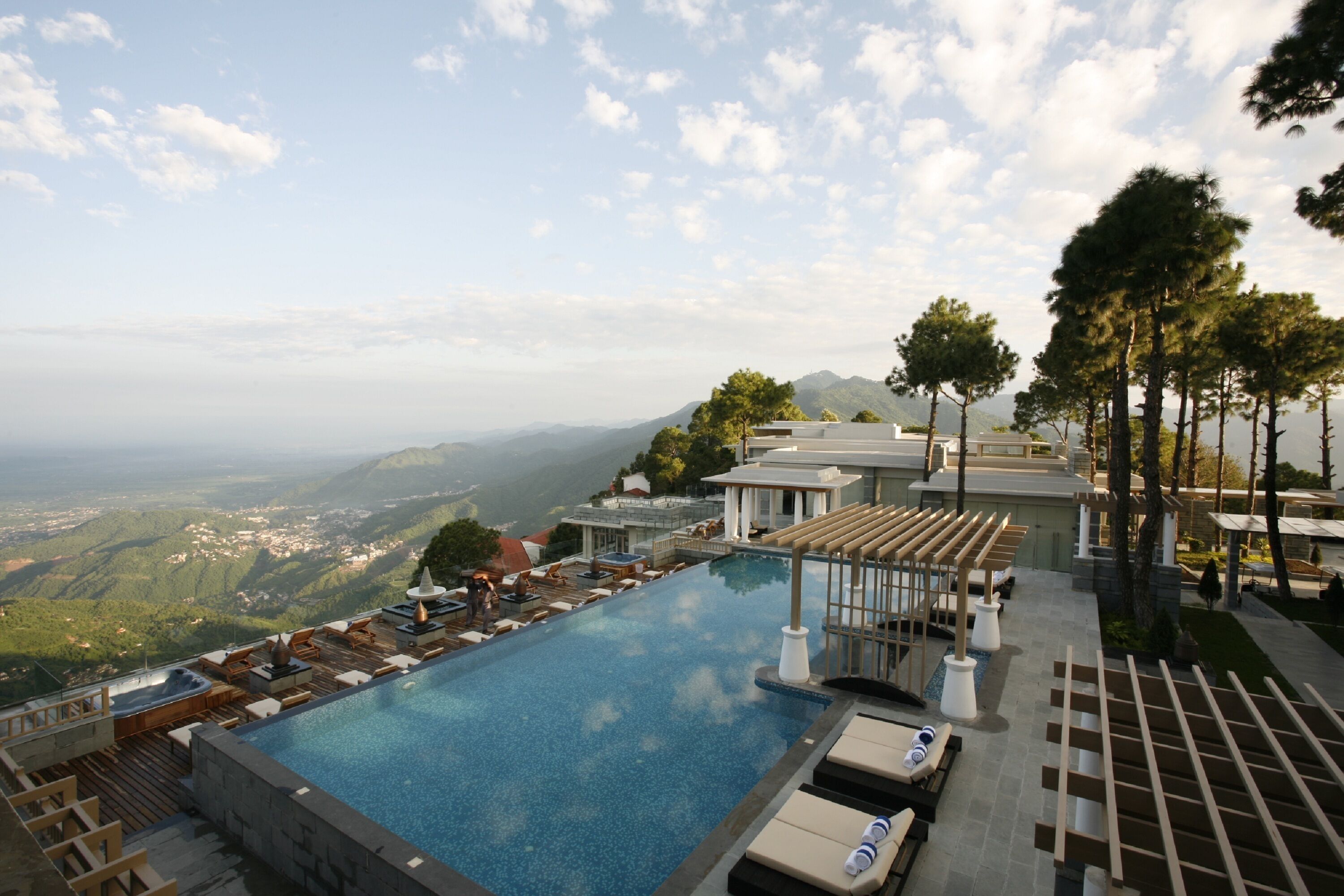 A rooftop infinity pool with lounge chairs and a view of the mountains.