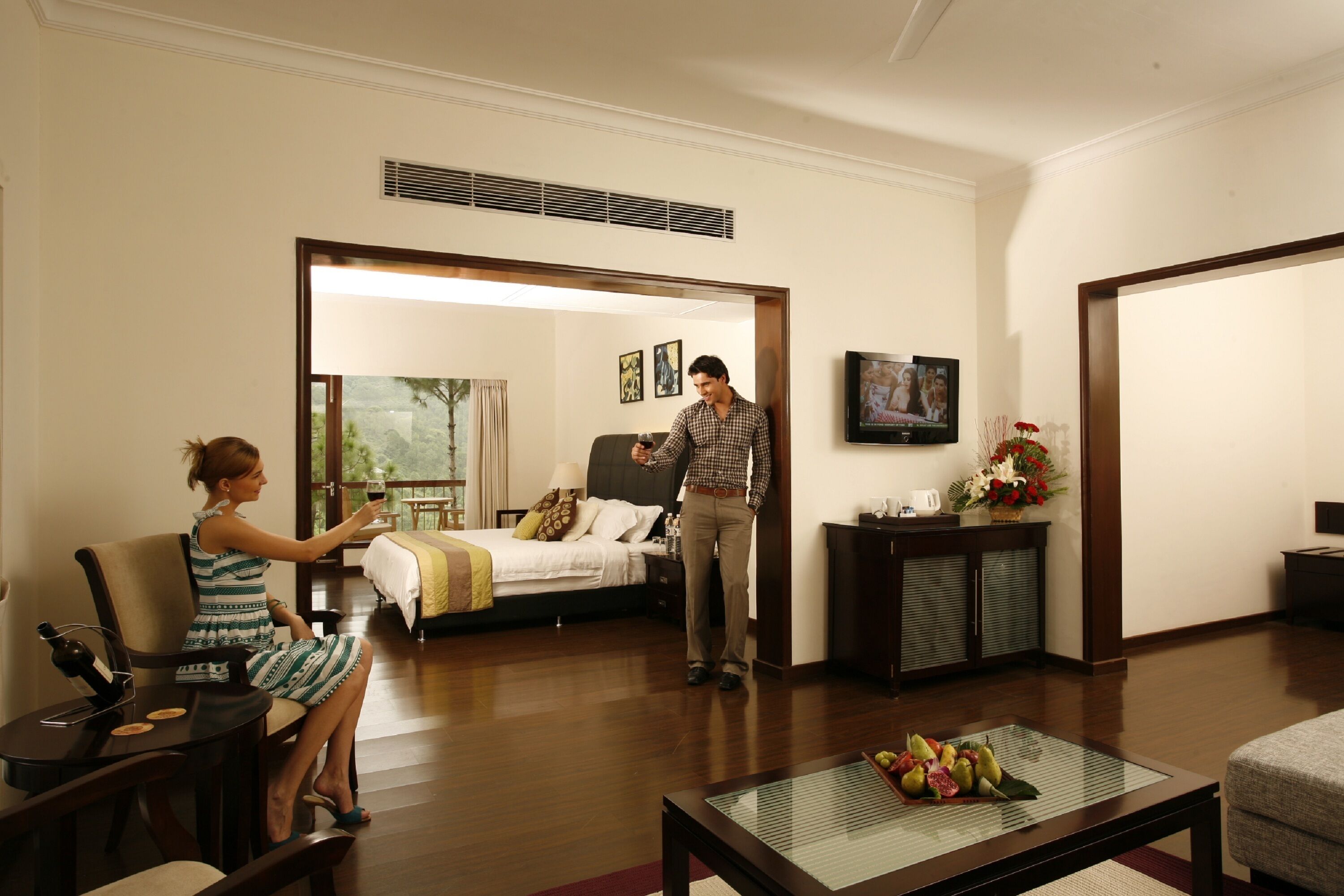 A hotel room with a bed, a sitting area with a table and chairs, a television, and a window with curtains.