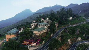 A mountainous area with a winding road and several buildings with green roofs. - Ayur County (Devikolam)