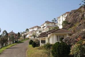 A residential area with houses on a hillside, a paved road, and well-maintained greenery. - Ayur County (Devikolam)