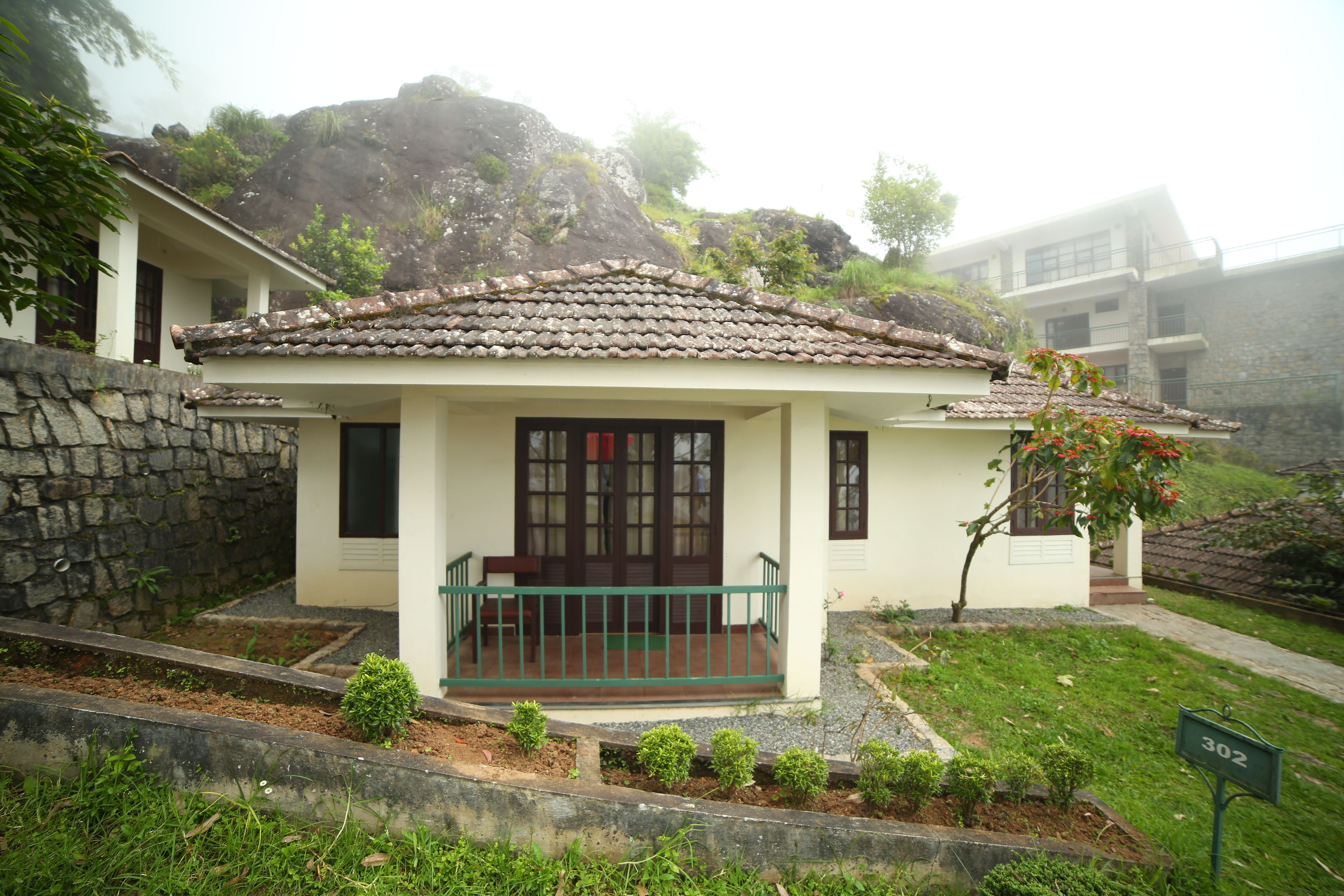 A single-story house with a tiled roof, a front porch, and a stone wall.