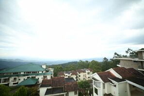 A residential area with multiple buildings, some with green roofs and others with red tiles, surrounded by greenery and mountains in the background. - Ayur County (Devikolam)