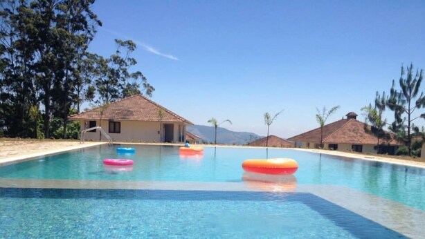 A clear swimming pool with three inflatable rings, surrounded by buildings with tiled roofs and palm trees. - Ayur County (Devikolam)
