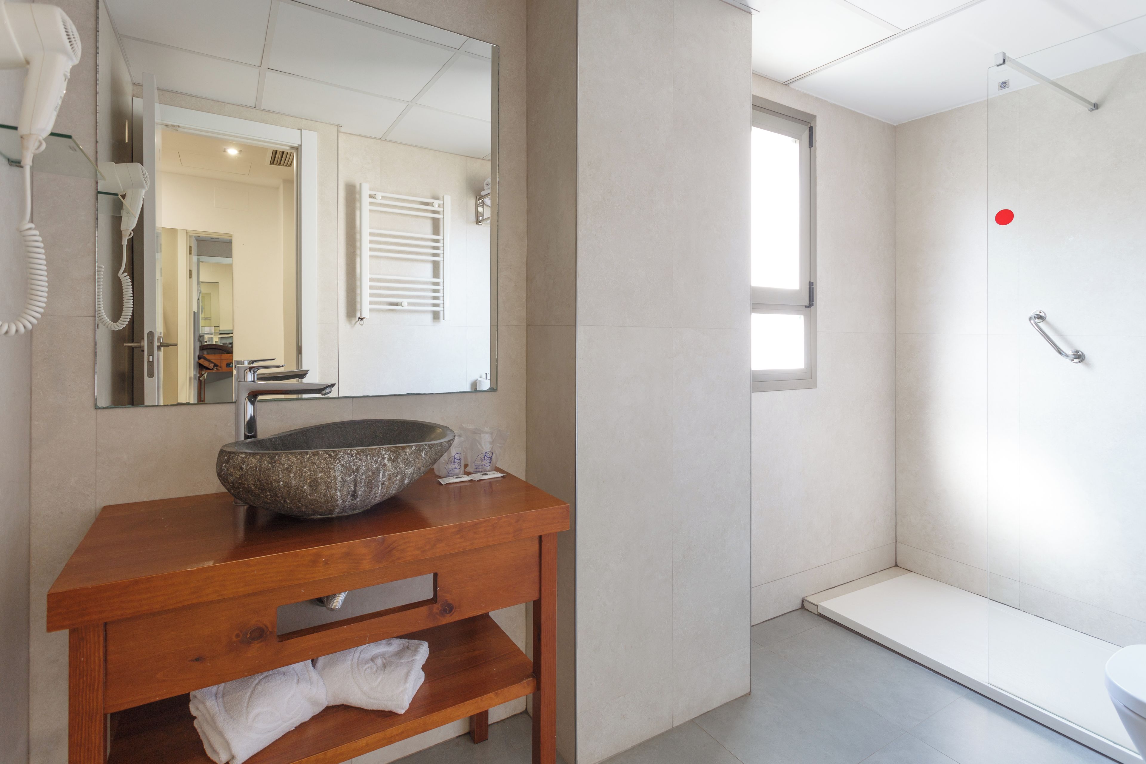 Un baño con tocador de madera, un espejo grande, un lavabo de piedra y una zona de ducha.