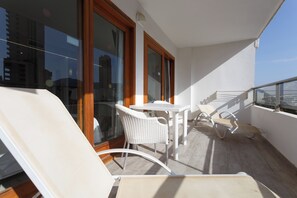 Un balcon doté de meubles en osier blanc, comprenant une table et deux chaises, et offrant une vue sur le paysage urbain.