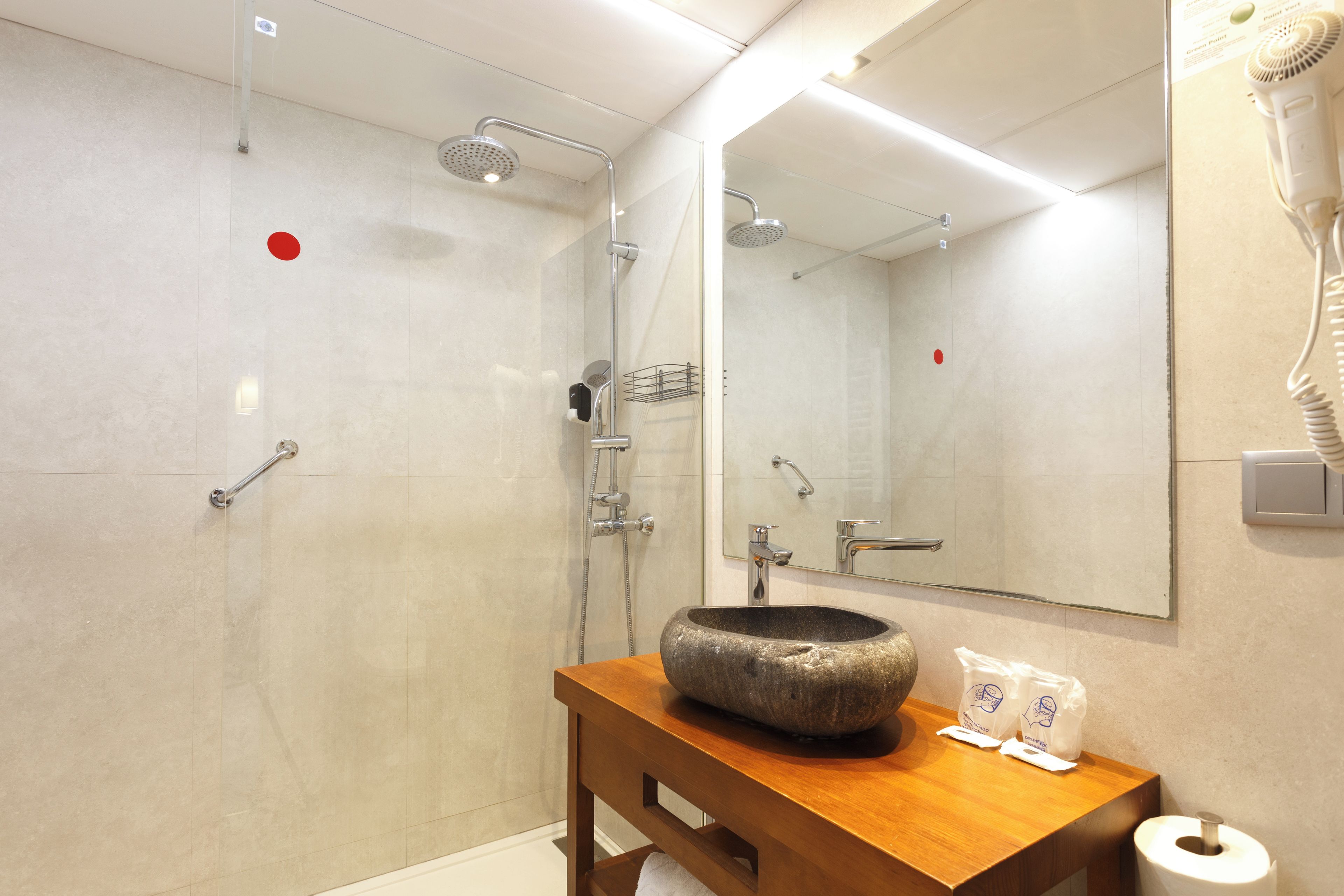 Een badkamer met een douche, een wastafel met een stenen waskom, een houten wastafelmeubel en een spiegel.