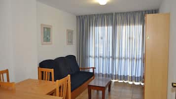 Una sala de estar con sofá, mesa de madera, sillas y un amplio ventanal con cortinas.