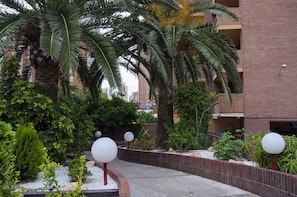 A landscaped area with palm trees, a brick building, and a gravel path. - Trebol One Apartments By Mc (Benidorm)
