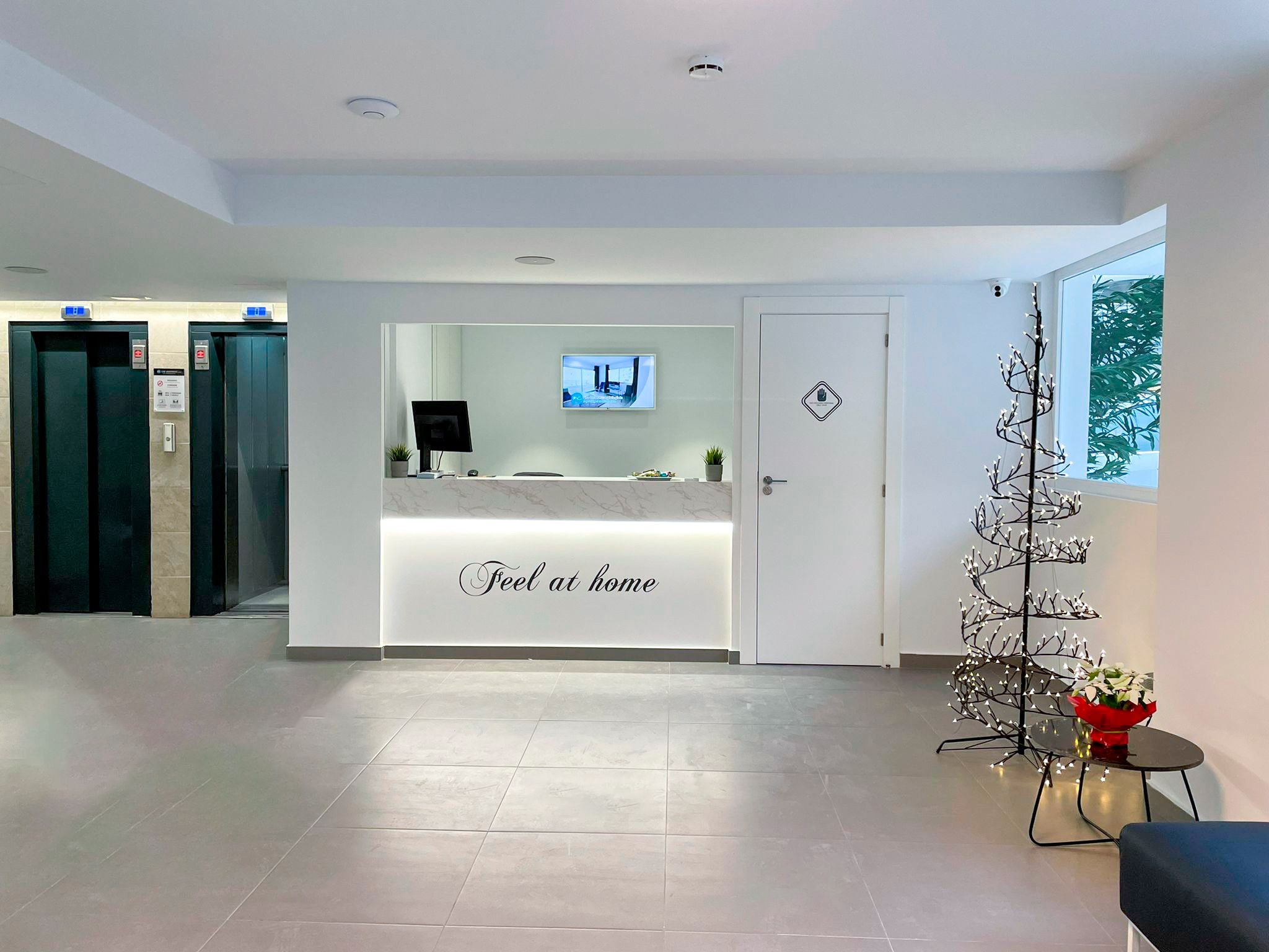 A reception area with a 'Feel at home' sign, a reception desk, a television, and a door with a hand symbol.