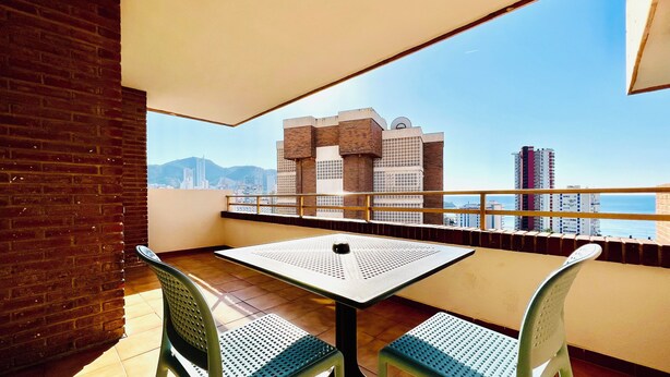 A balcony with a table and chairs, offering a view of a cityscape and mountains. - Trebol One Apartments By Mc (Benidorm)
