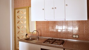 Una cocina con estufa a gas, pileta y alacenas blancas.
