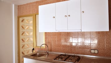 Una cocina con estufa a gas, pileta y alacenas blancas.
