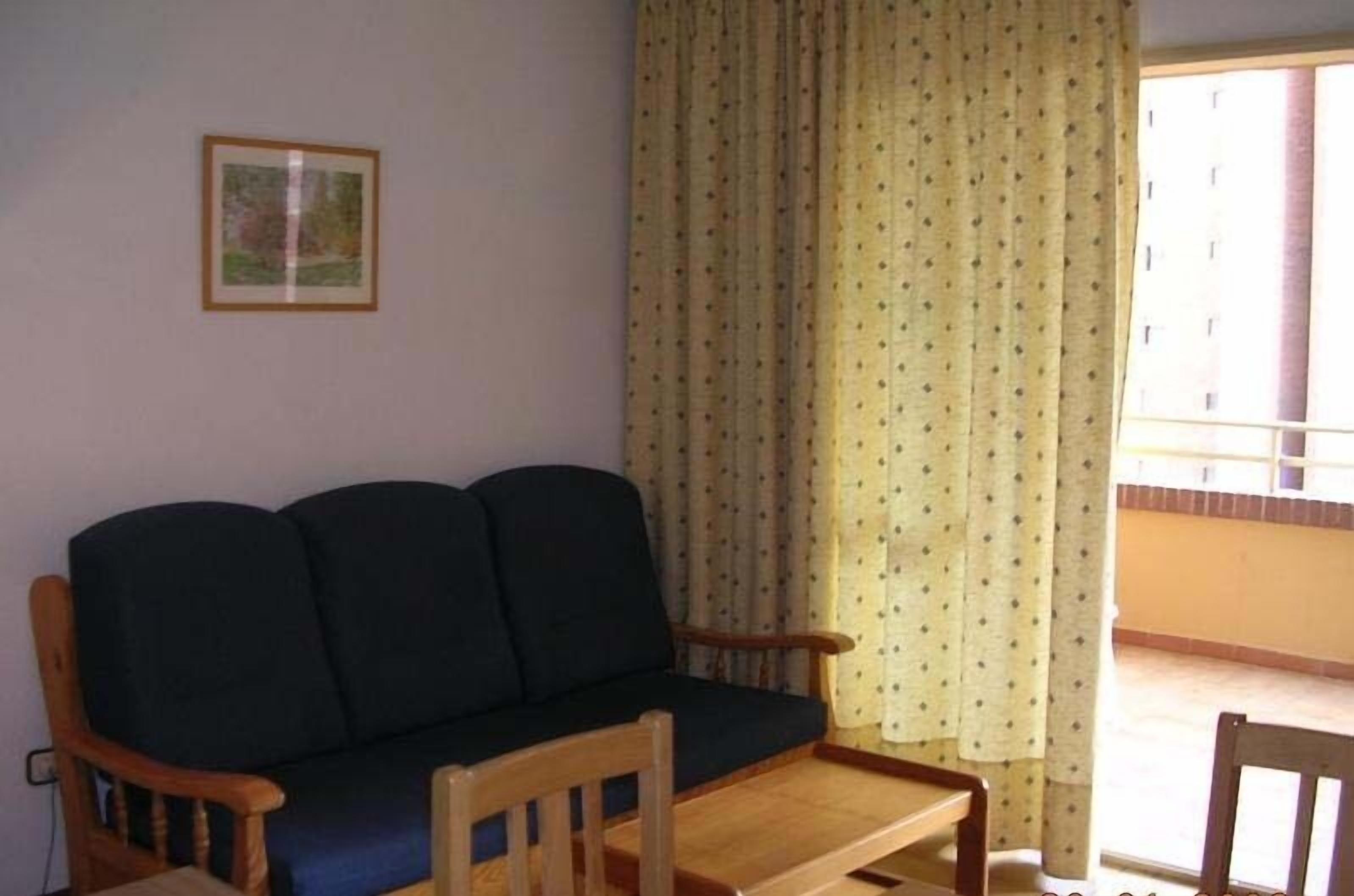A living room with a sofa, wooden chairs, a small table, and a window with curtains.