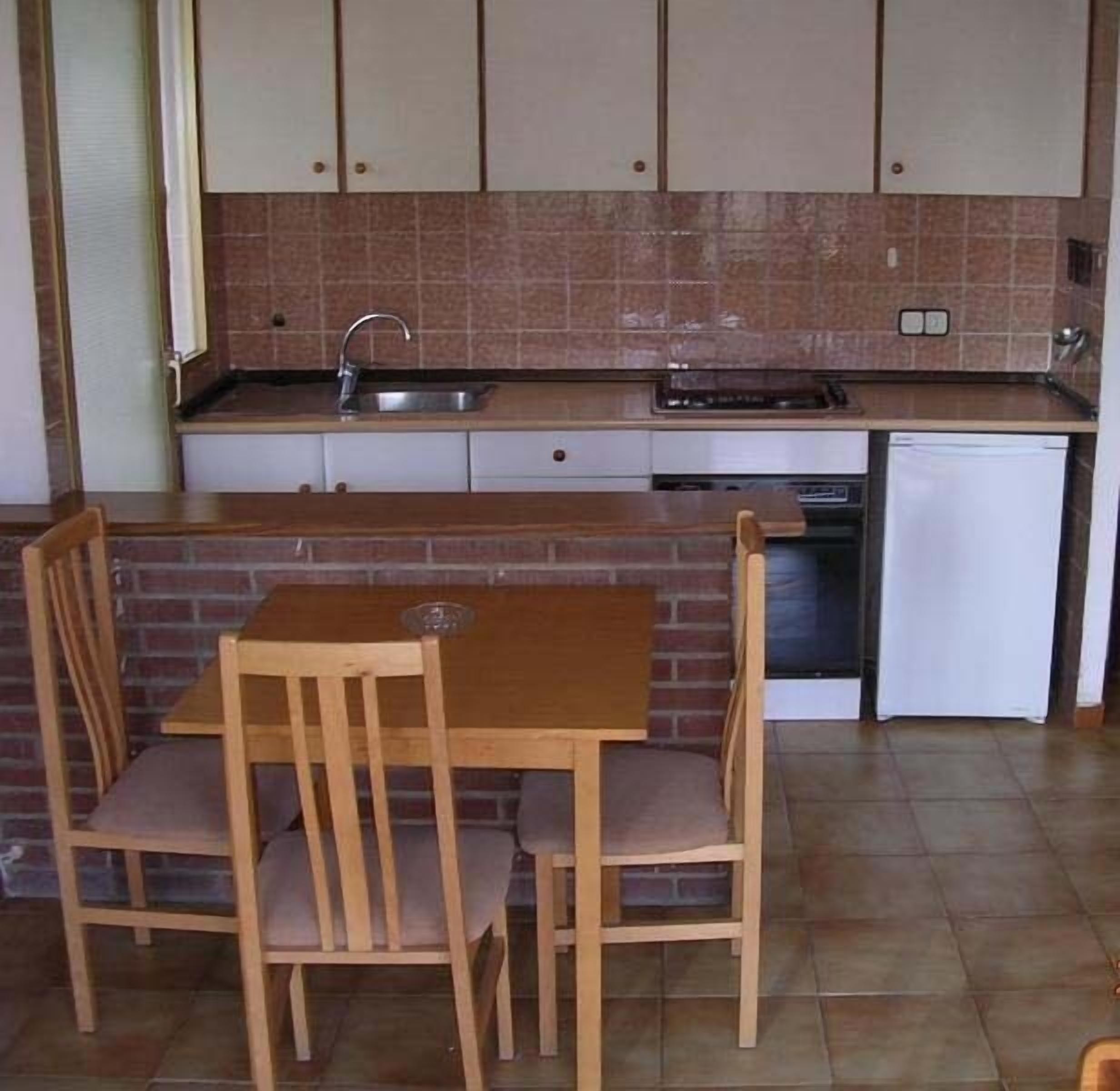 Cocina compacta con lavaplatos, estufa y lavavajillas. Hay una mesa de madera y dos sillas.