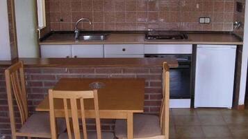 Cocina compacta con lavaplatos, estufa y lavavajillas. Hay una mesa de madera y dos sillas.
