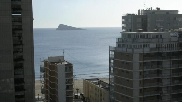 Un paisaje costero con rascacielos, una vista despejada del mar y una isla distante.