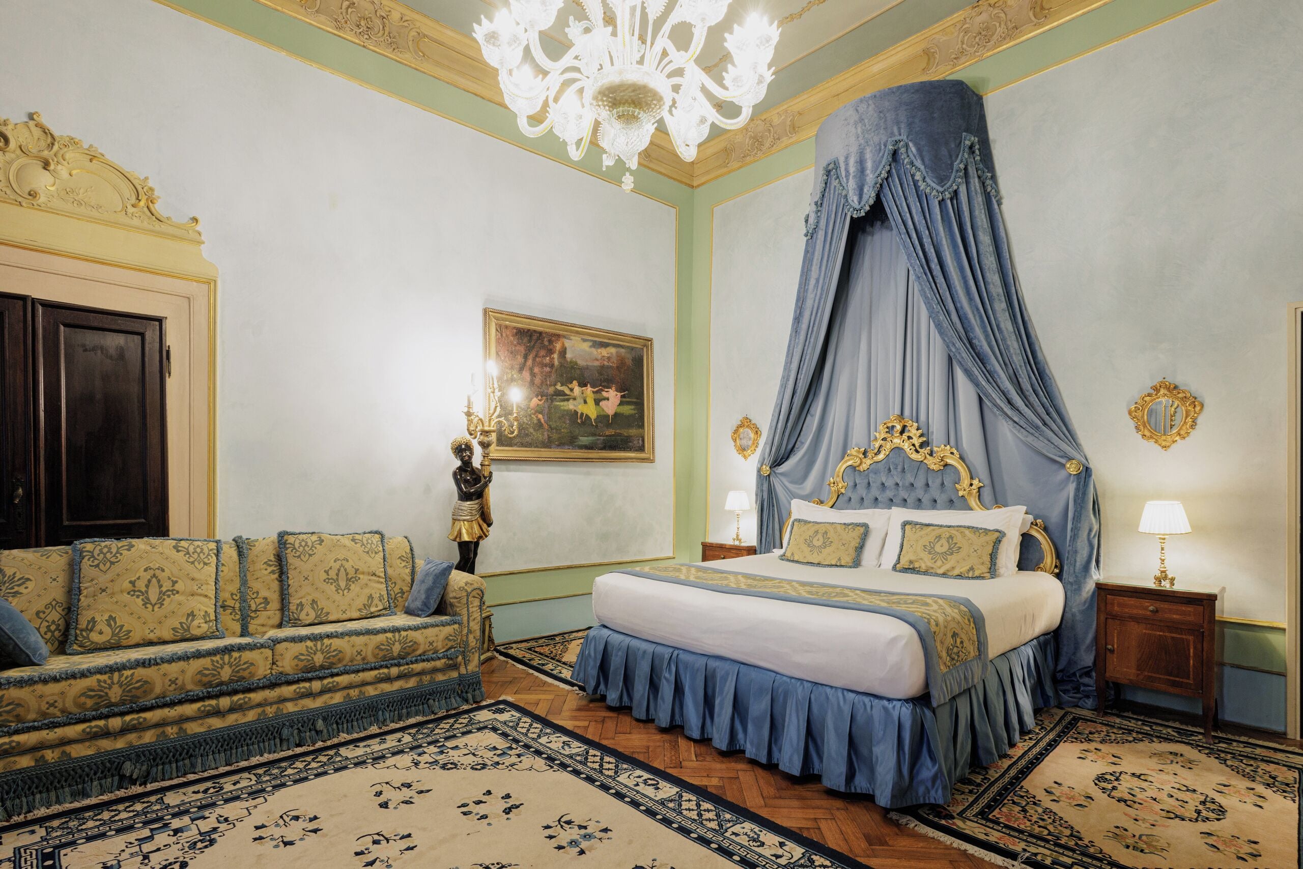 A bedroom with a four-poster bed, a sofa, a chandelier, and a painting on the wall.