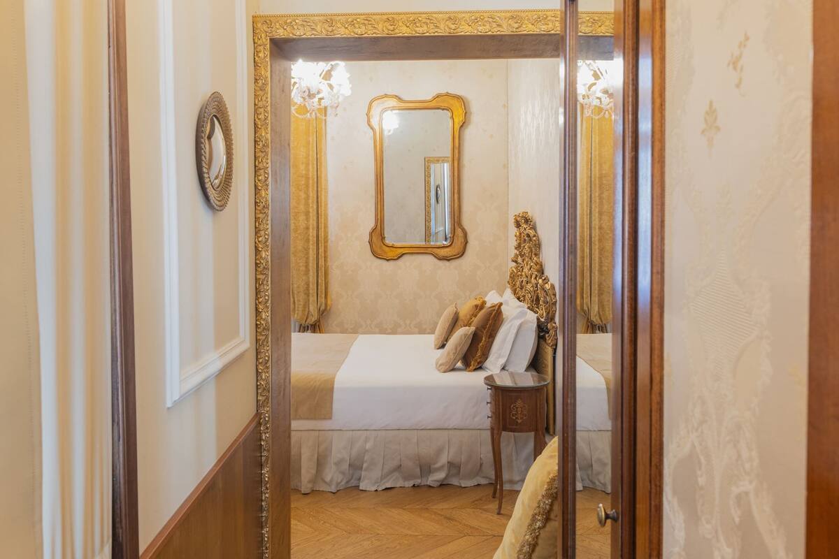A hotel room with a bed, a nightstand, a mirror, and a chandelier.