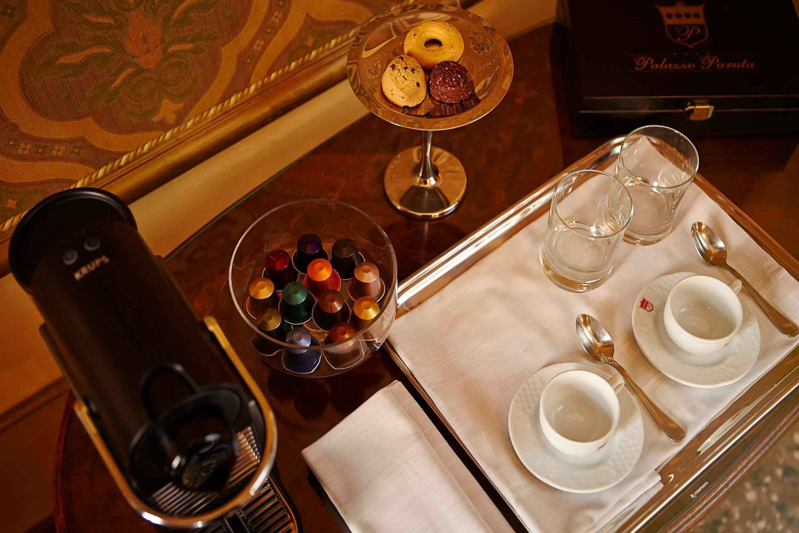 Una bandeja con un plato de postre, una cafetera, un tazón de bombones y dos tazas con sus platillos.