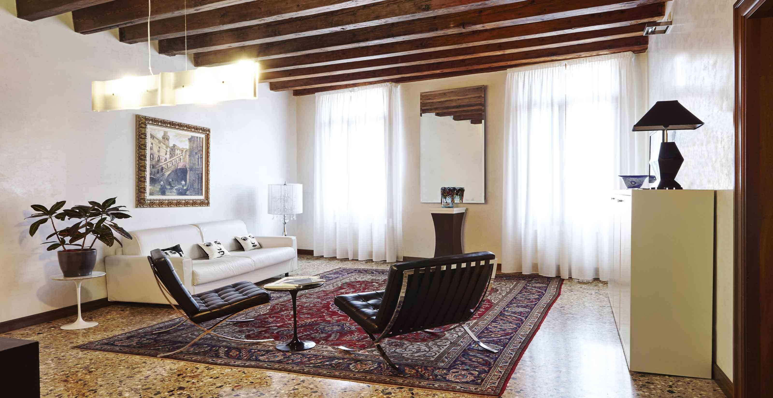 Una sala de estar con un sofá, dos sillones, una mesa de centro, una alfombra, una planta en maceta, un cuadro, una lámpara, un espejo y un aparador.