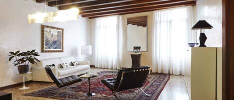 Una sala de estar con un sofá, dos sillones, una mesa de centro, una alfombra, una planta en maceta, un cuadro, una lámpara, un espejo y un aparador.