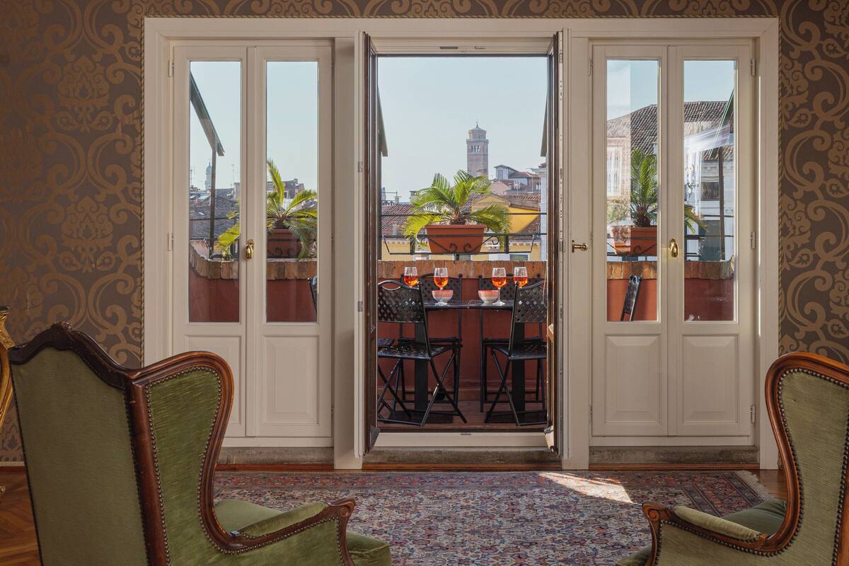 A room with a view of a cityscape through a glass door, featuring two chairs and a table with wine glasses.