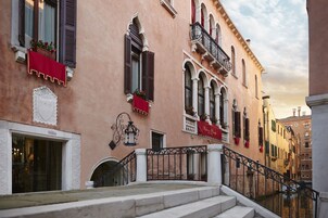 Una calle estrecha con edificios que tienen balcones, ventanas con contraventanas y un canal.