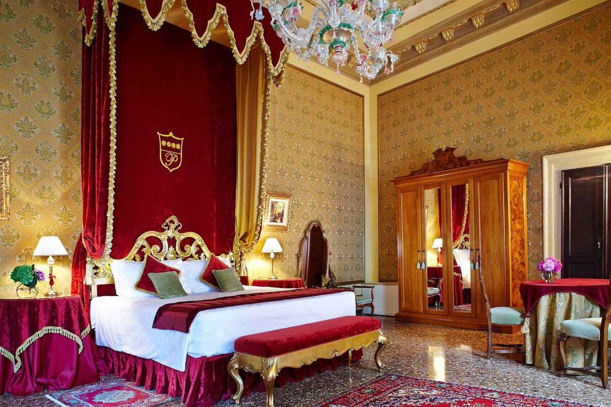 A luxurious hotel room with a large bed, a wooden wardrobe, and a chandelier.