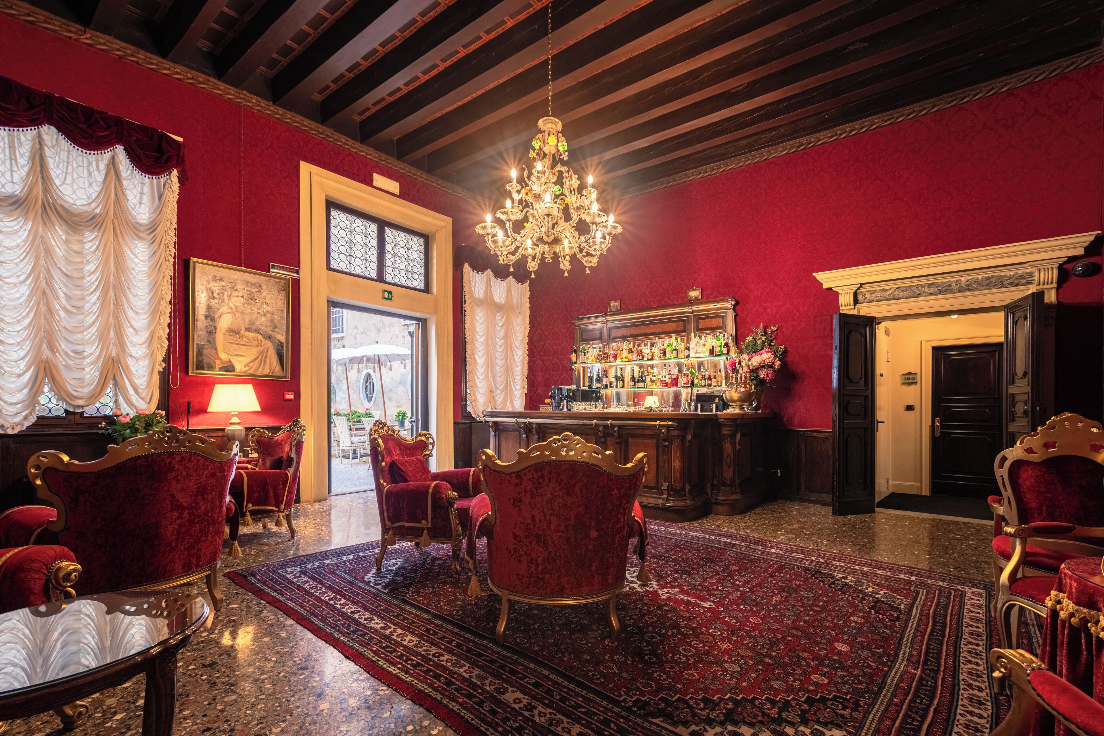 A luxurious lobby with red walls, ornate chandeliers, and classic red velvet chairs.