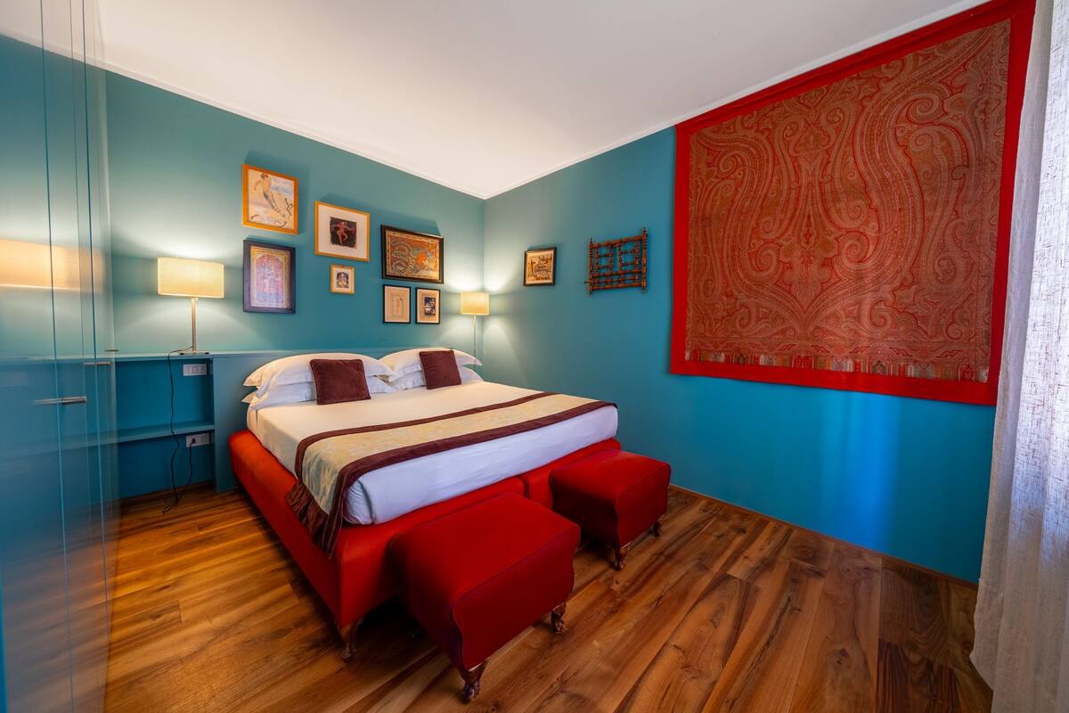 A bedroom with a bed, red upholstered benches, a blue wall, and framed pictures.
