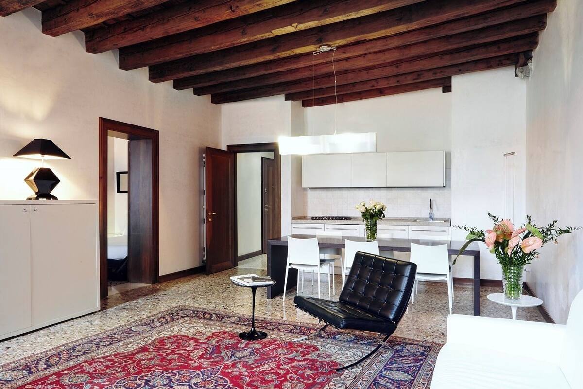 A modern interior with a wooden ceiling, a dining area with chairs, a sofa, and a patterned rug.