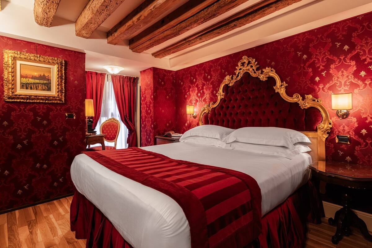 A room with a large bed, red walls, a wooden ceiling, and a framed picture on the wall.