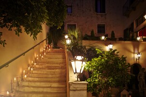 Una escalera con varios peldaños, rodeada de plantas en macetas e iluminada por lámparas de pared.