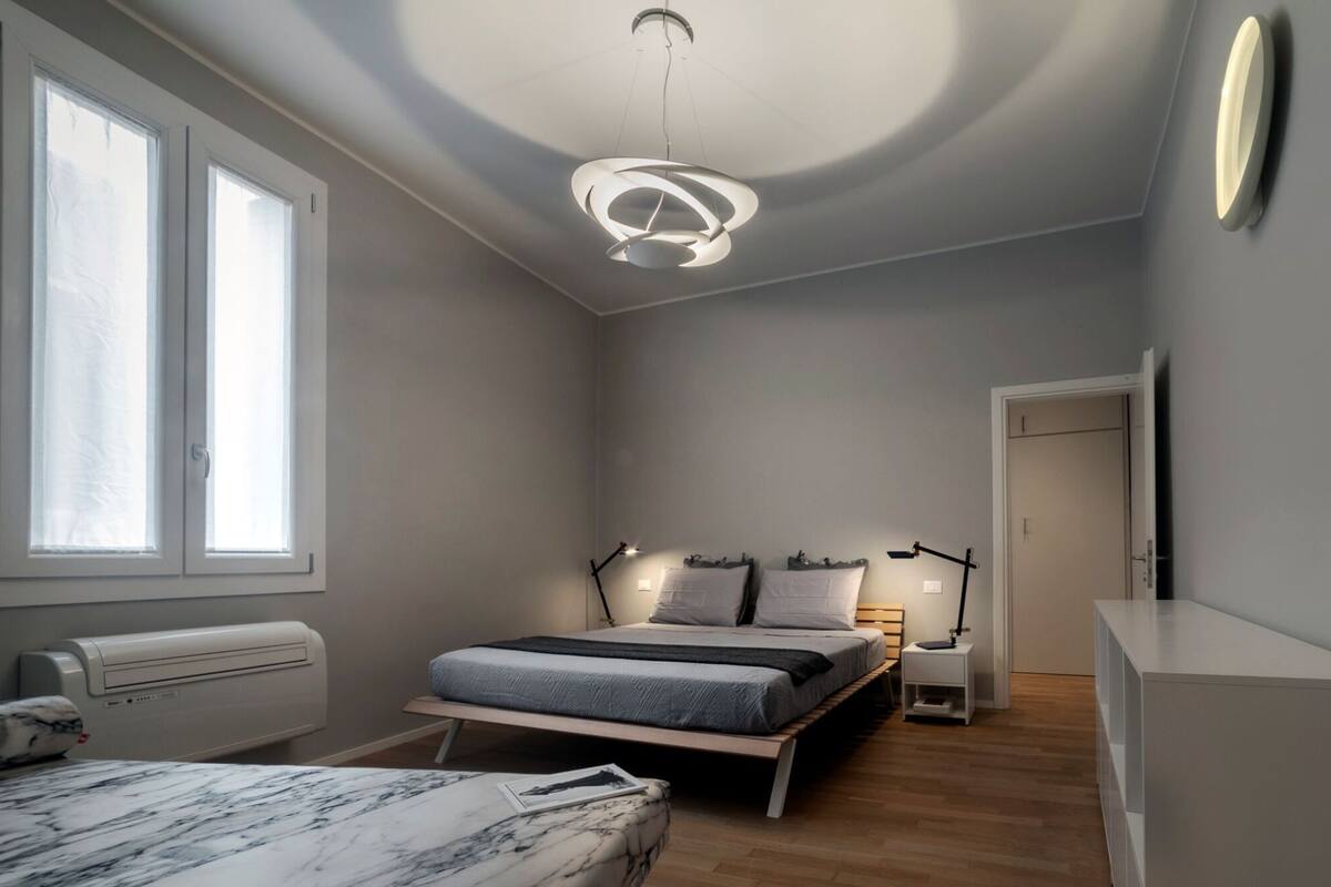 A bedroom with a bed, bedside tables, a desk, a chair, a heater, and a window.