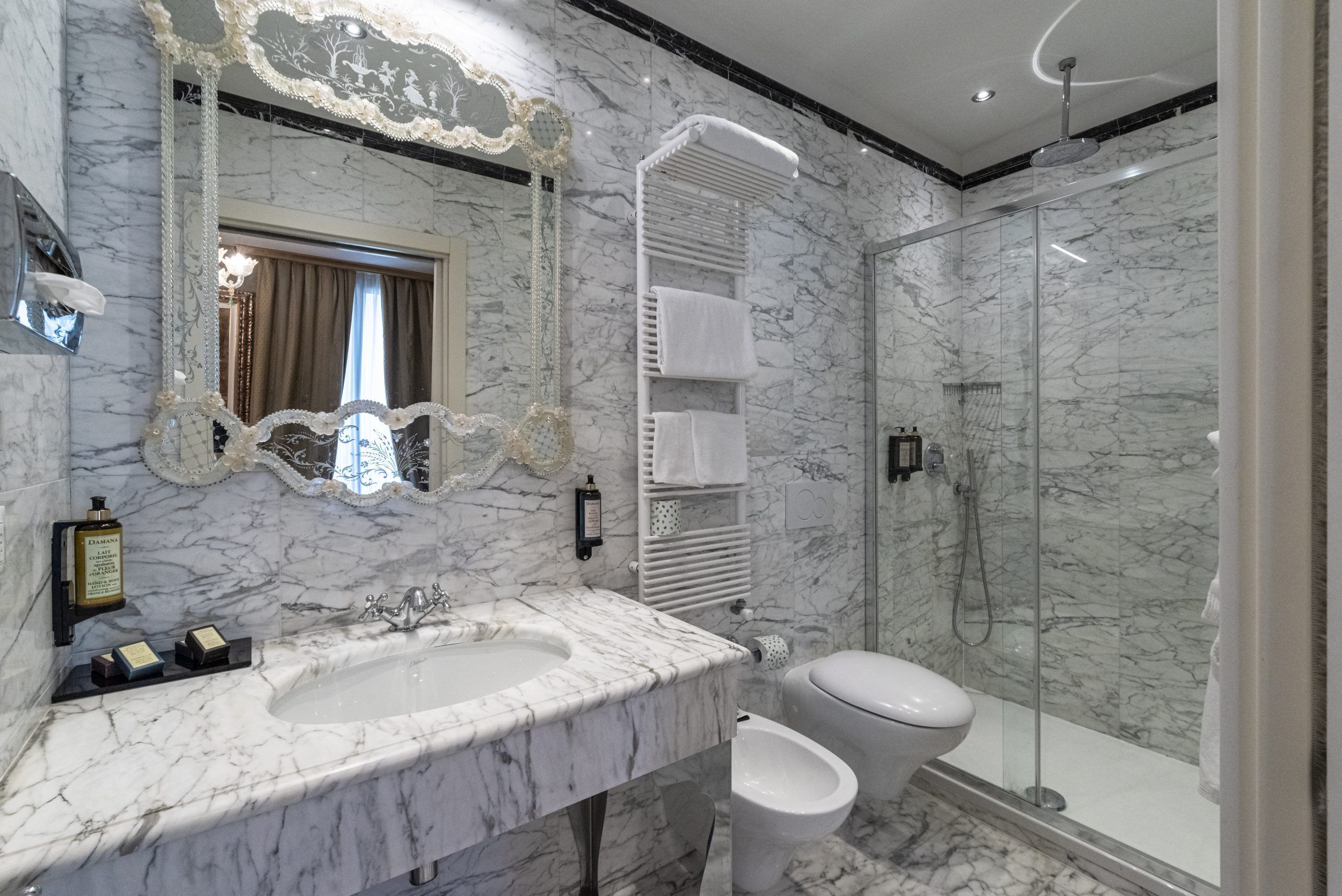 A bathroom with a marble sink, a toilet, a glass shower enclosure, and a decorative mirror.