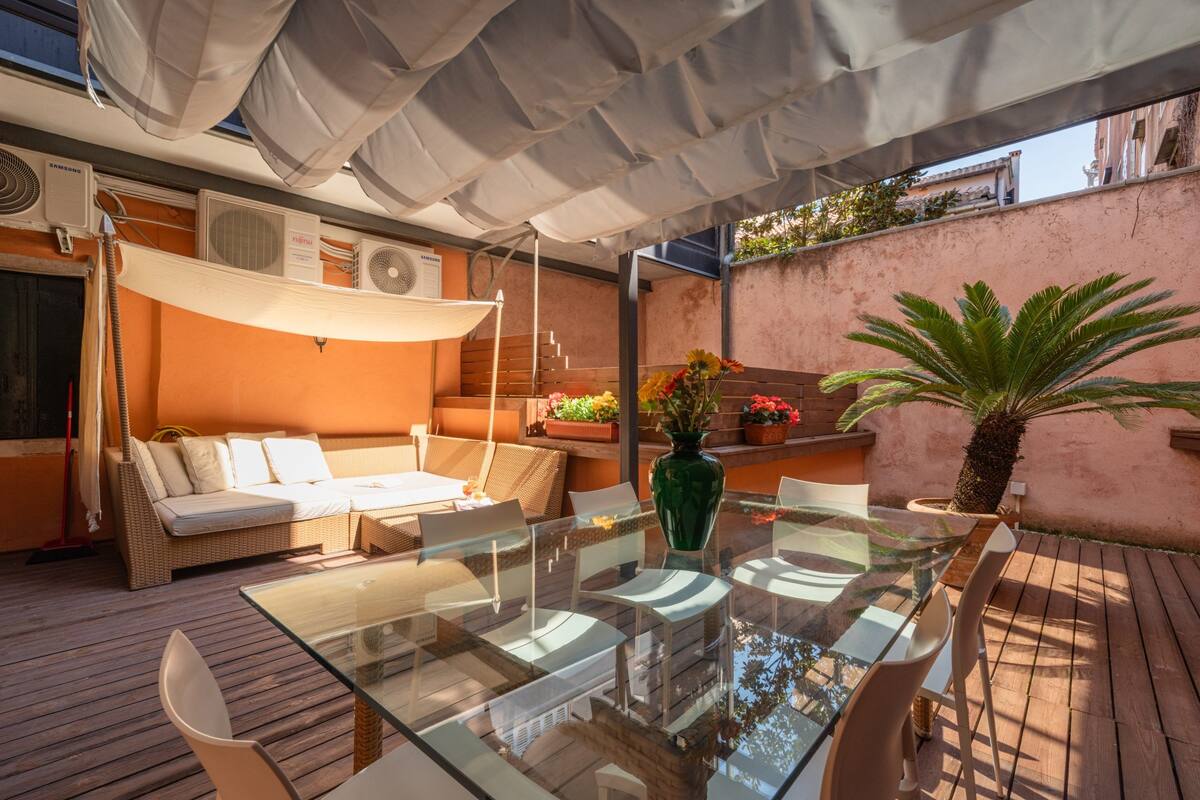 An outdoor patio with a glass table, wicker furniture, and a potted plant.