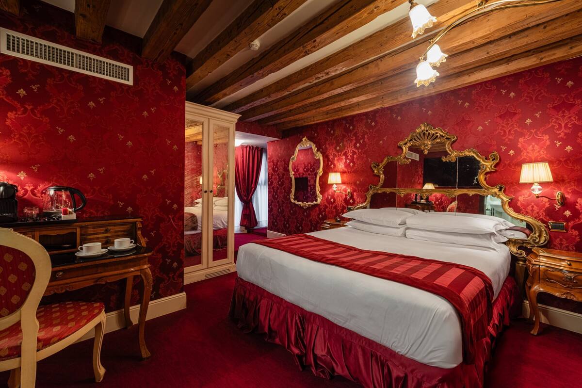 A room with a large bed, wooden ceiling beams, a mirror, and a desk with a chair.