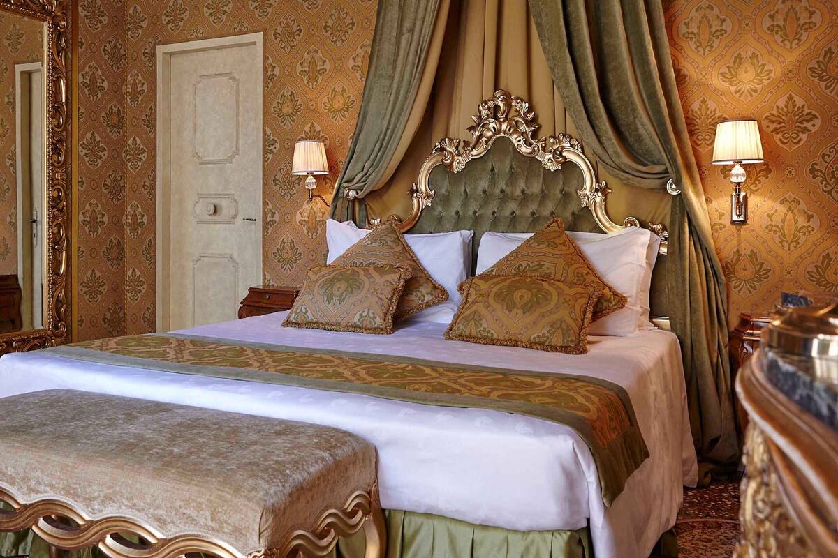 A four-poster bed with ornate headboard, two bedside lamps, and a bench at the foot of the bed.