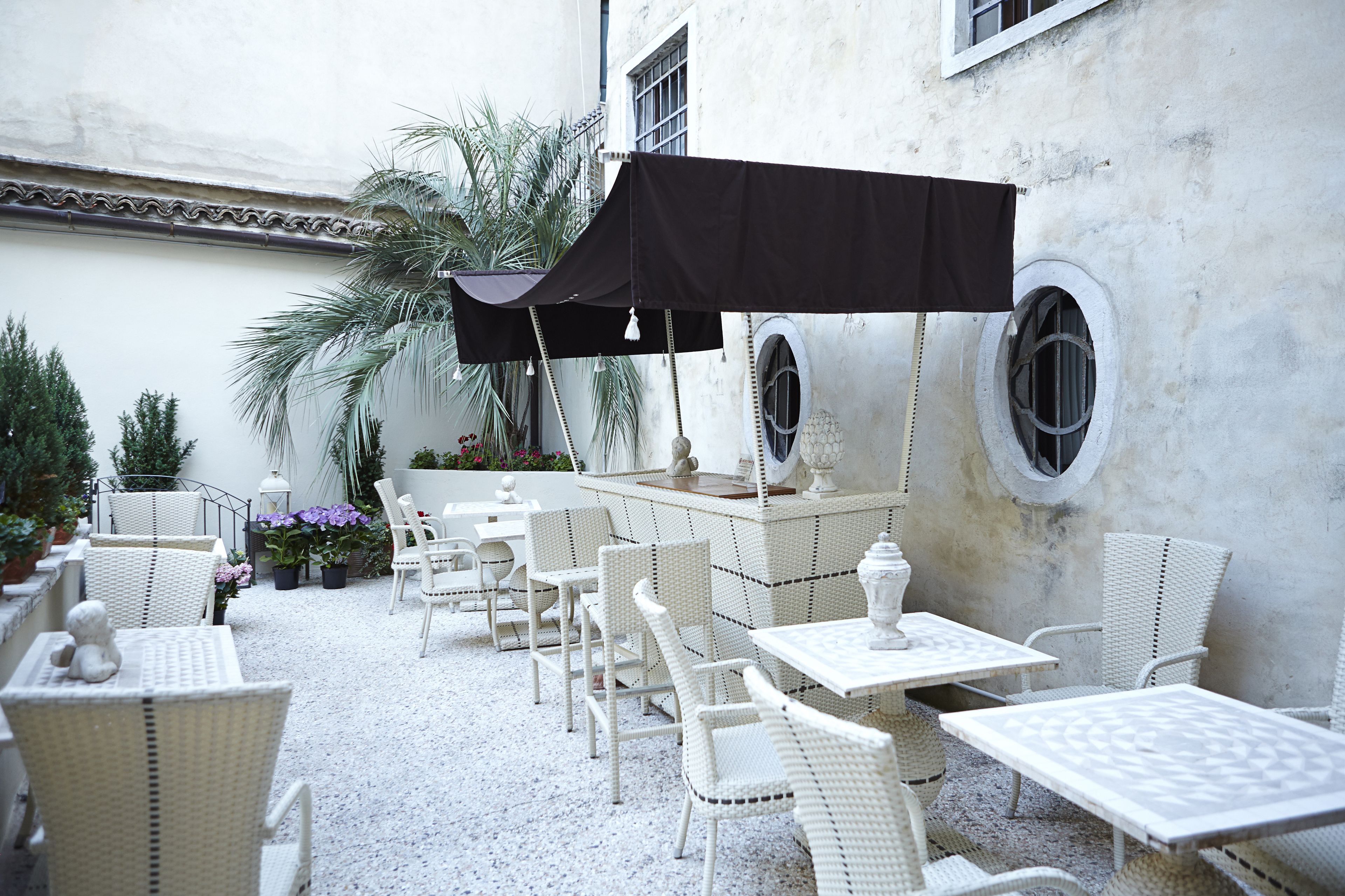 An outdoor patio with white wicker furniture, a black umbrella, and a decorative fountain.