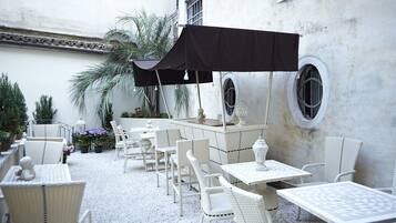 An outdoor patio with white wicker furniture, a black umbrella, and a decorative fountain.