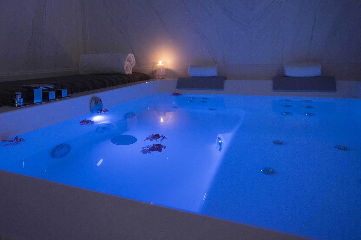 A spa bath with a blue light, a towel, and a small table with a candle.