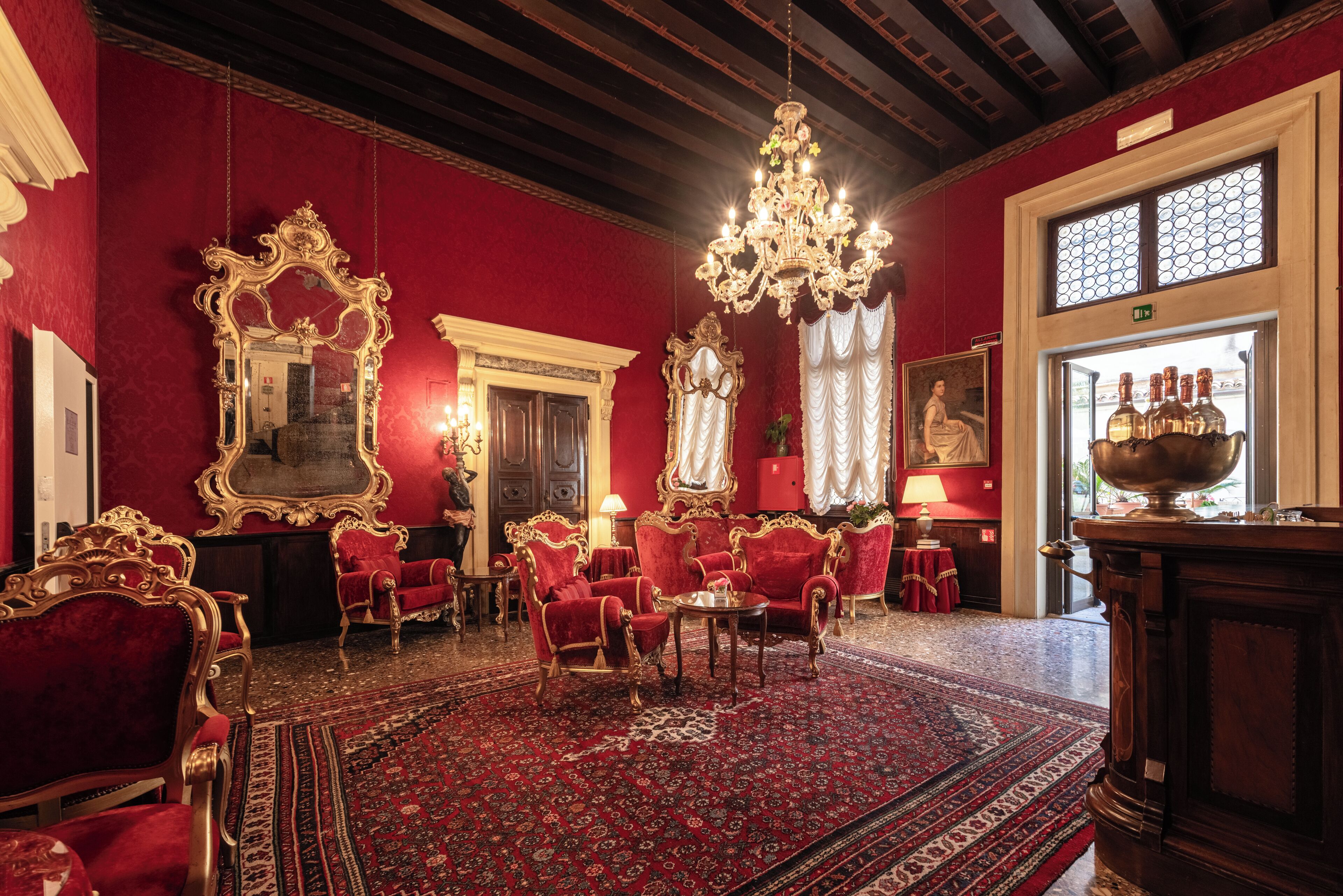 A luxurious room with red walls, ornate gold furniture, a chandelier, and a large mirror.