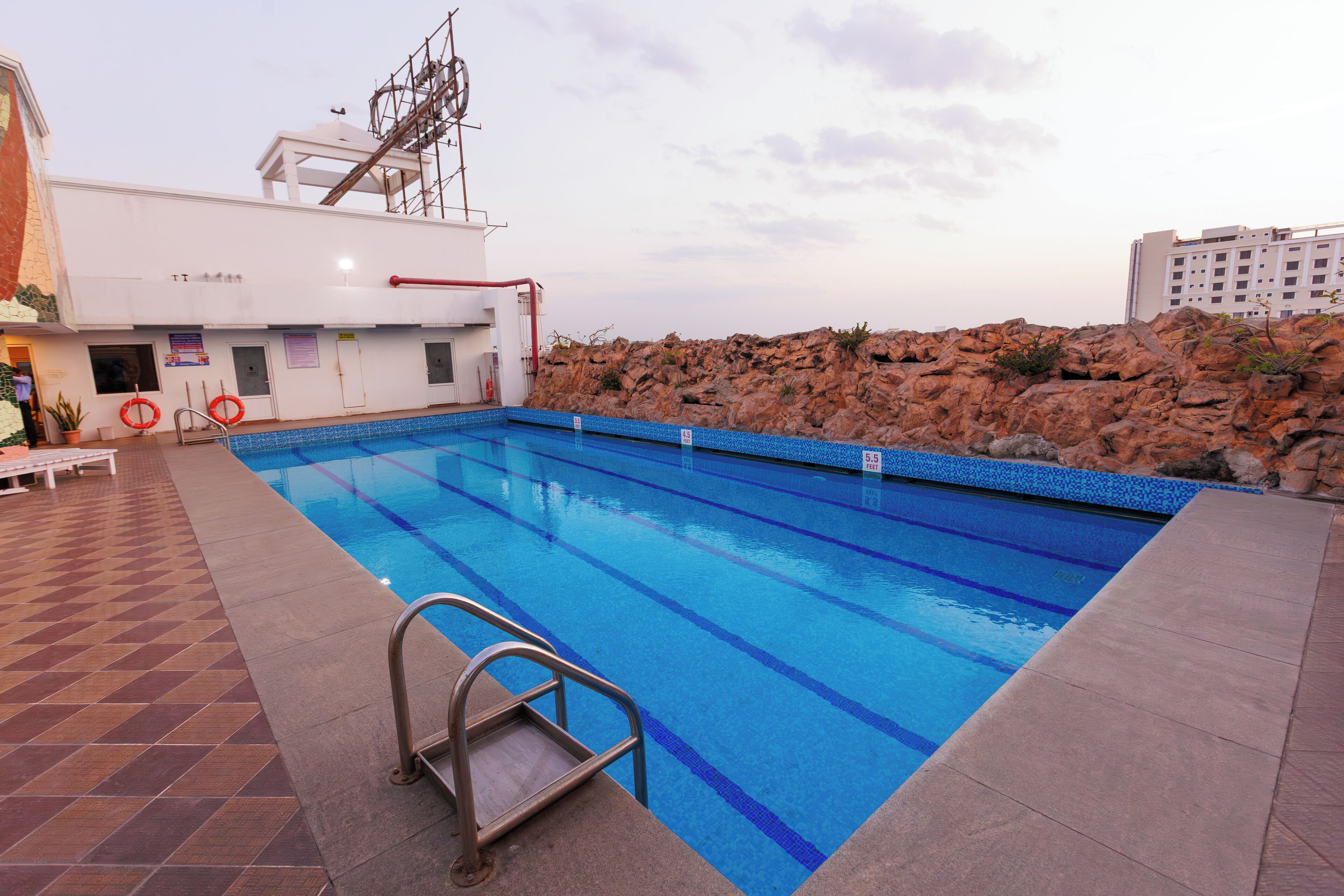 A swimming pool with clear blue water, a lifeguard chair, and a rocky hillside in the background.